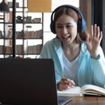 A young woman waves at meeting attendees at a Zoom meeting.